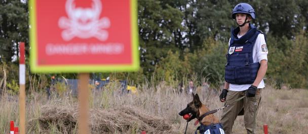 woman handler with a dog, next to the sign stop mines